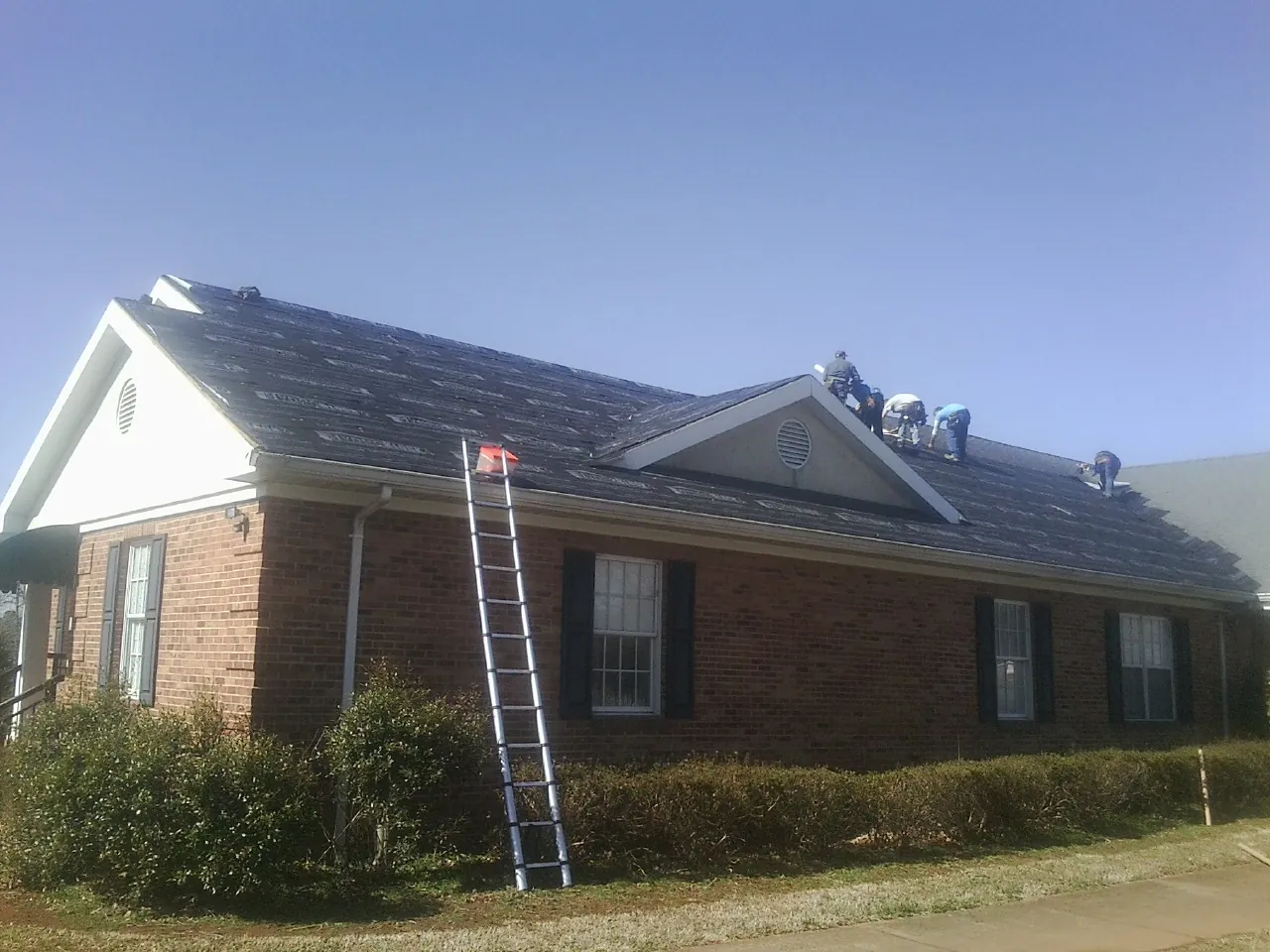 Crew tearing shingles off a brick ranch roof with a ladder set — Metal Roof Repair work by our crew in Jeffersonville